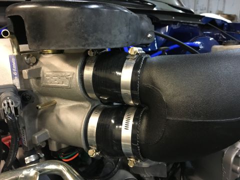 1996 Ford Bronco - A close-up view of a silver BBK intake manifold with two black silicone hoses connected via hose clamps. The manifold has the BBK logo embo…