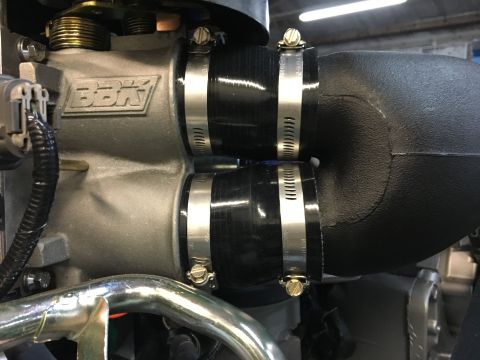 1996 Ford Bronco - A close-up view of a BBK throttle body with two black silicone intake hoses attached with silver hose clamps. The intake hoses connect to a…