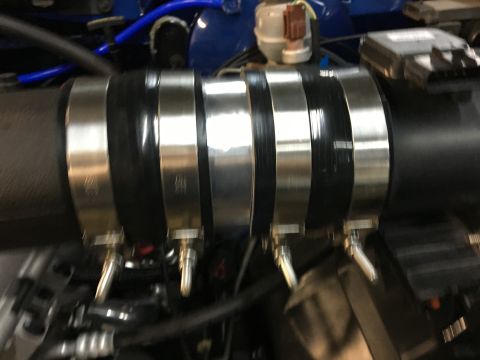 1996 Ford Bronco - A close-up view of a black intake hose secured with four metal hose clamps. The hose and clamps are part of a vehicle's engine bay.
