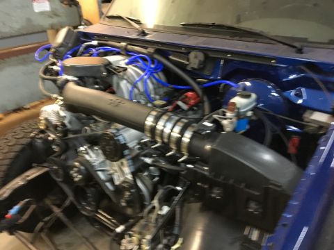 1996 Ford Bronco - The engine bay of a blue vehicle, likely a 1996 Ford Bronco, is shown with various engine components and blue vacuum lines visible.
