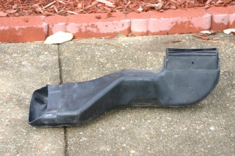 1996 Ford Bronco - A black plastic air intake duct is shown lying on a concrete surface. The duct has a rectangular opening at one end and a wider, curved ope…