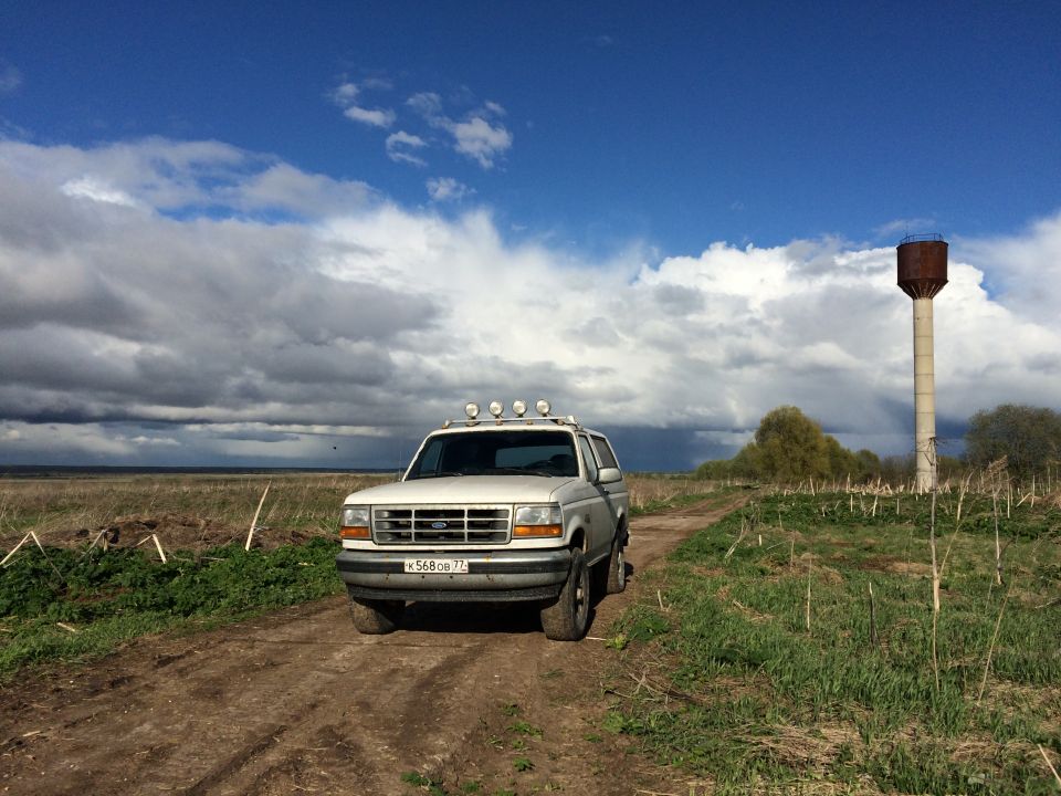 White 1993 Ford Bronco on a dirt road with a water tower in the background.