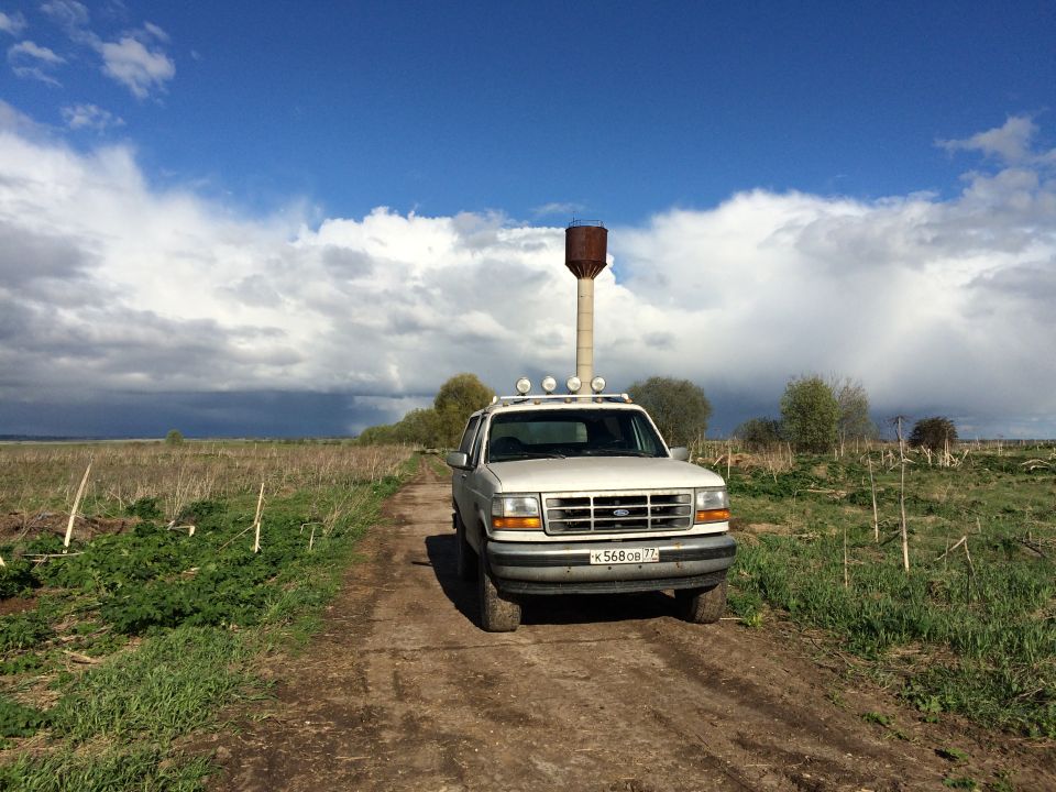White 1993 Ford Bronco on a dirt road with a water tower.