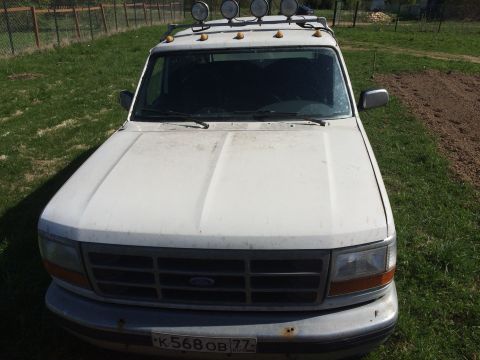 1993 Ford Bronco - A white Ford Bronco is parked on a grassy area next to a dirt patch. The vehicle has a roof rack with two large spotlights and a license pl…