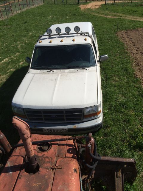 1993 Ford Bronco - A white 1990s Ford pickup truck with four auxiliary lights mounted on the roof rack is parked on a grassy area next to a dirt field. The fr…