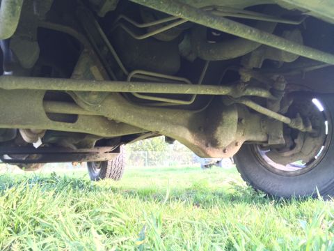 1993 Ford Bronco - The underside of a 1993 Ford Bronco shows the rear differential, suspension components, and a tire. The vehicle is parked on grass.