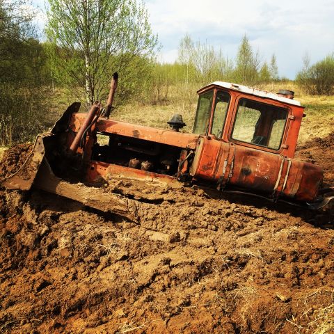 1993 Ford Bronco - An old, orange tractor with a front loader is stuck in thick mud with trees and a cloudy sky in the background.