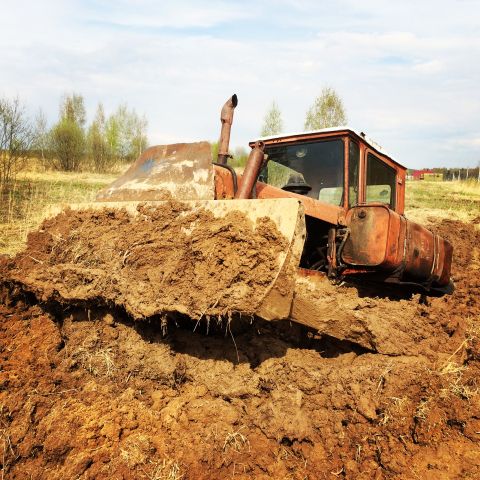 1993 Ford Bronco - An old, rusty orange tractor is pushing a large mound of wet mud and dirt, with trees and a cloudy sky in the background.