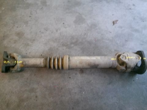 1996 Ford Bronco - A driveshaft with U-joints at both ends and a rubber boot in the middle is laid out horizontally on a concrete surface. Yellow markings are…