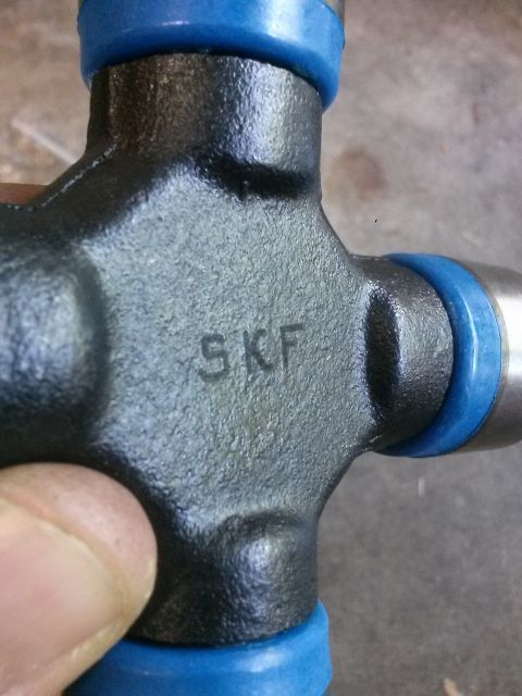 1996 Ford Bronco - A close-up shot shows a black u-joint with blue seals, featuring the embossed text "SKF" on its central body. The part is held by a person'…