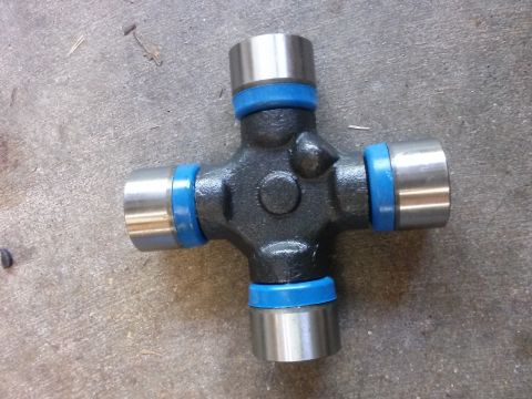 1996 Ford Bronco - A universal joint part with a dark gray cross-shaped body and four silver cylindrical ends, each with a bright blue rubber seal. The part i…