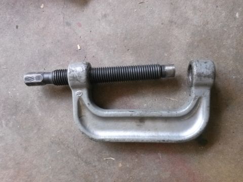 1996 Ford Bronco - A C-clamp tool is shown lying on a concrete surface. The clamp is made of gray metal and has a threaded screw mechanism.