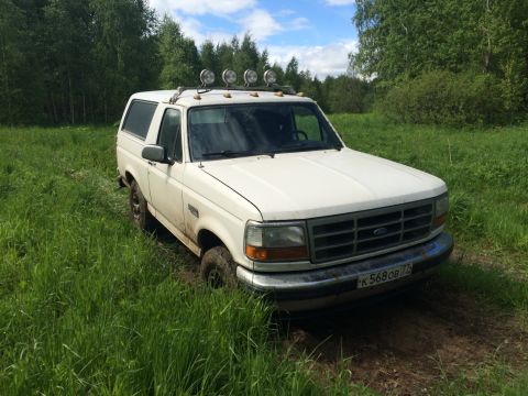 1993 Ford Bronco - A white Ford Bronco is parked in a grassy field with trees in the background. The vehicle has four auxiliary lights mounted on the roof rac…