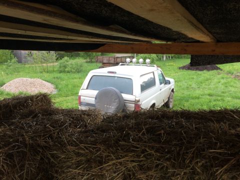 1993 Ford Bronco - A white Ford Bronco is parked in a grassy field, viewed from behind a pile of hay. The vehicle has a spare tire cover on the rear and a lig…