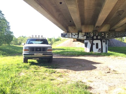 1993 Ford Bronco - A white Ford Bronco is parked under a concrete overpass with graffiti on its support pillars. The vehicle is facing forward, showing its fr…
