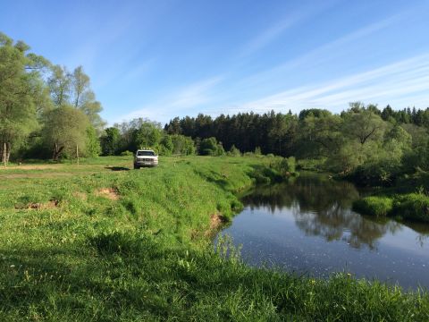 1993 Ford Bronco - A white Ford van is parked on a grassy field next to a winding river under a clear blue sky with wispy clouds.