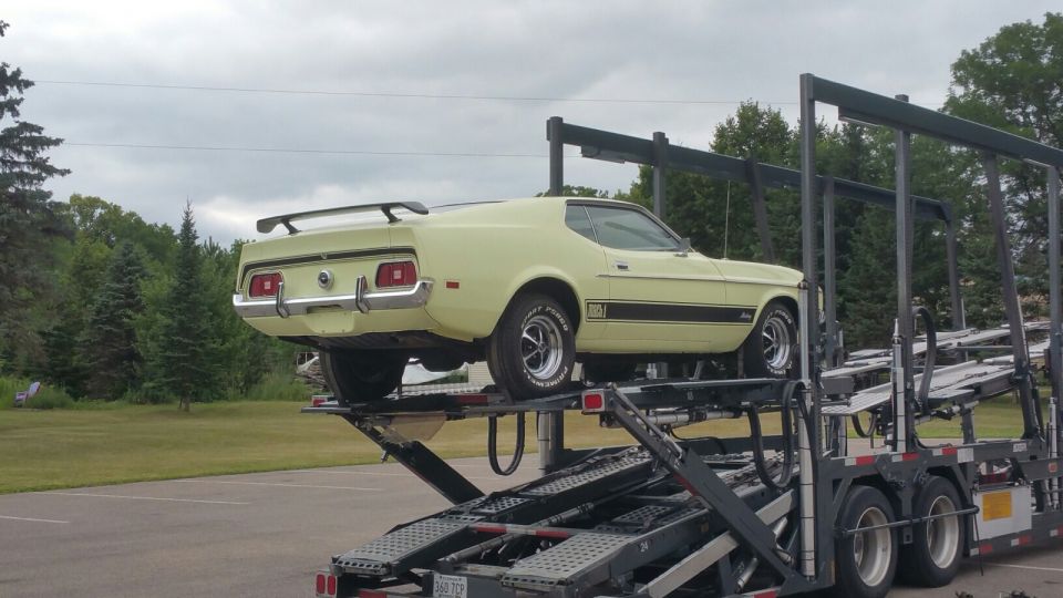 Pale yellow 1971 Ford Mustang Mach 1 on a car carrier, rear quarter view.