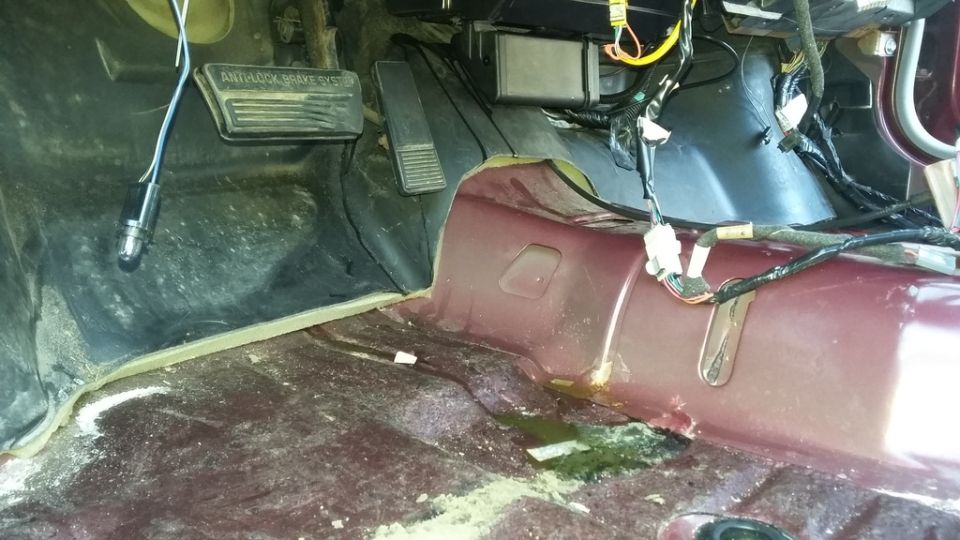 Interior of a car's footwell with pedals and exposed wiring.