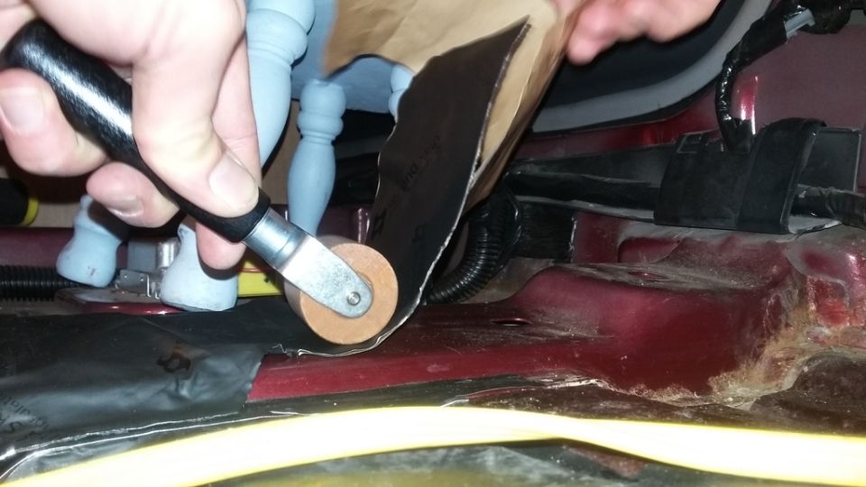 Applying sound deadening material to car floor with roller tool