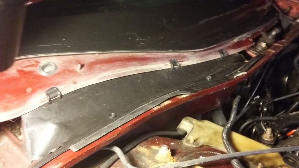 Close-up of a red vehicle's cowl area with a black plastic panel and clips.