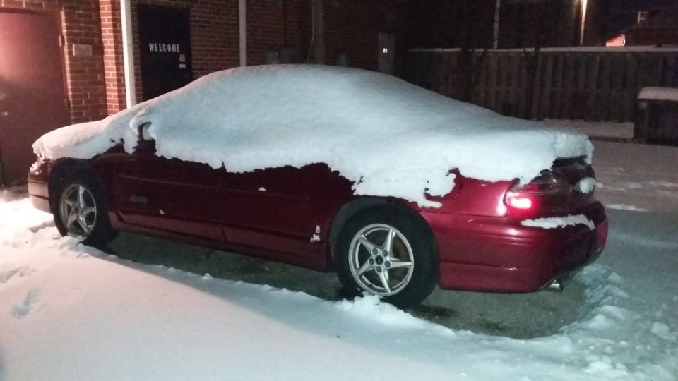 Red Pontiac Grand Prix covered in snow, parked outside a building at night.