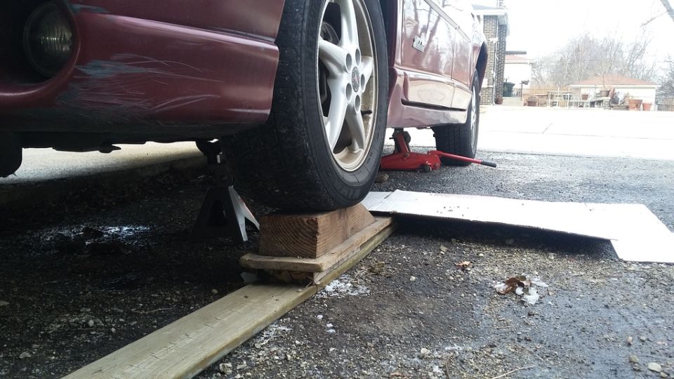 Red 2000 Pontiac Grand Prix on jack stands with wooden blocks and ramp under front tire.
