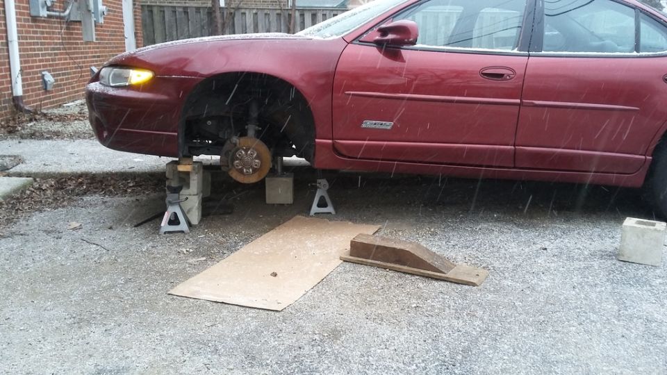 Maroon sedan on jack stands with front wheel removed in a driveway