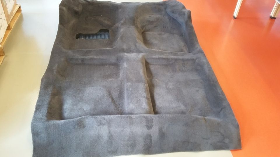 Dark gray molded car floor carpet laid out flat.