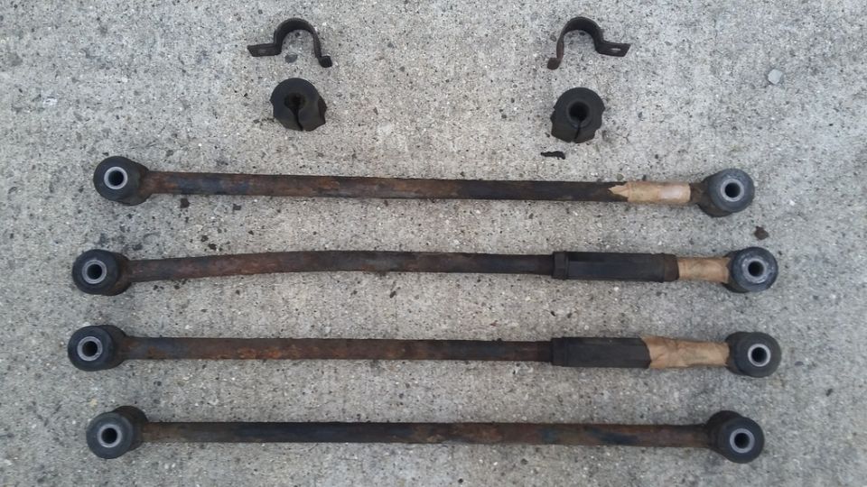 Four rusty stabilizer links with rubber bushings and mounting hardware on concrete.