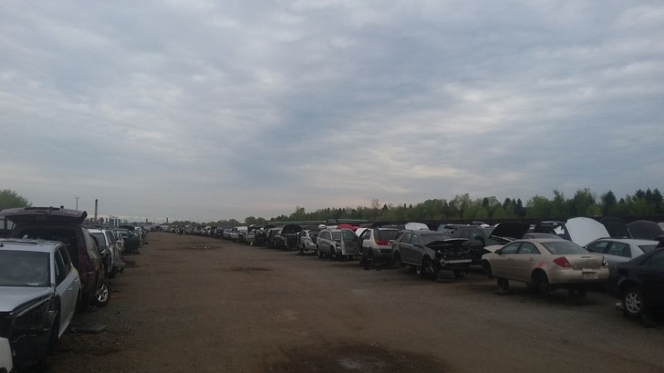 Junkyard with rows of cars, many with hoods open, under a cloudy sky.