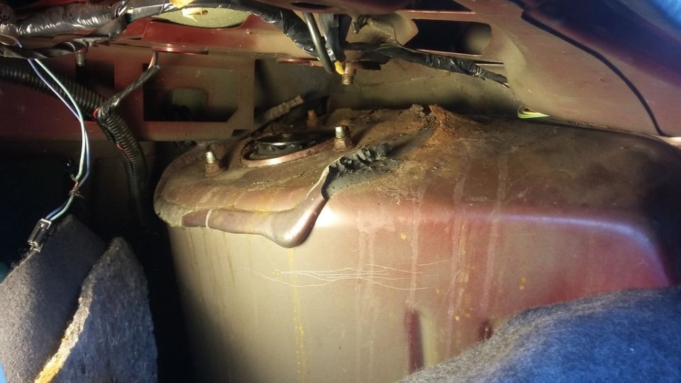 Rusty fuel tank with exposed wiring and mounting bolts, viewed from above