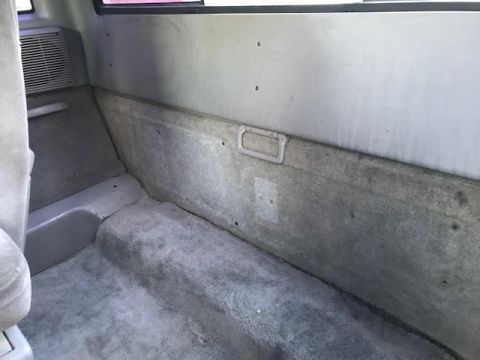 1986 Ford Bronco - The rear interior of an older SUV shows worn carpet and a side vent.