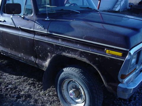 1992 Ford Bronco - A dark brown pickup truck is shown from the front quarter angle, revealing rust spots and a chrome bumper.