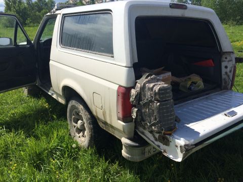 1993 Ford Bronco - Rear view of a white Ford Bronco with its tailgate down, showing a camouflage backpack and other items inside.