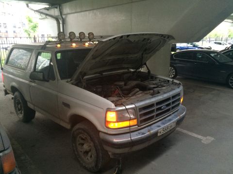 1993 Ford Bronco - A white 1993 Ford Bronco is parked with its hood open, revealing the engine and equipped with roof-mounted lights.