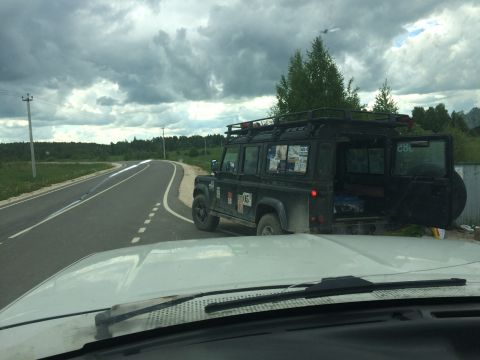 1993 Ford Bronco - A black Land Rover Defender 110 is parked on the side of a road with its rear doors open.