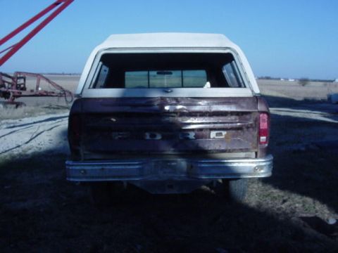 1992 Ford Bronco - Rear view of a weathered Ford truck, showing its tailgate and chrome bumper, with a white camper shell.