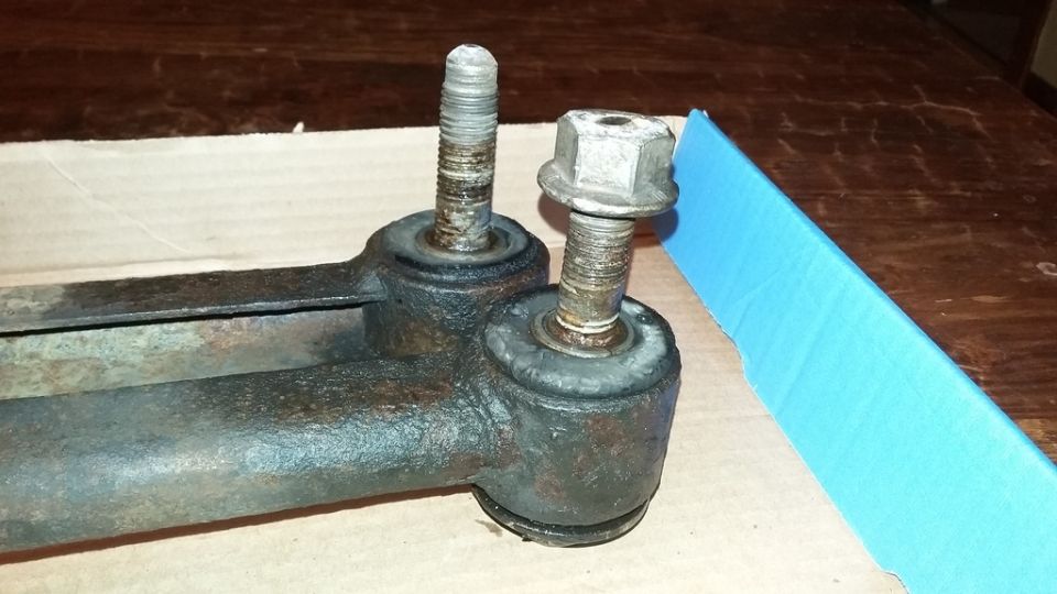 Close-up of a rusty suspension part with two bolts and rubber bushings