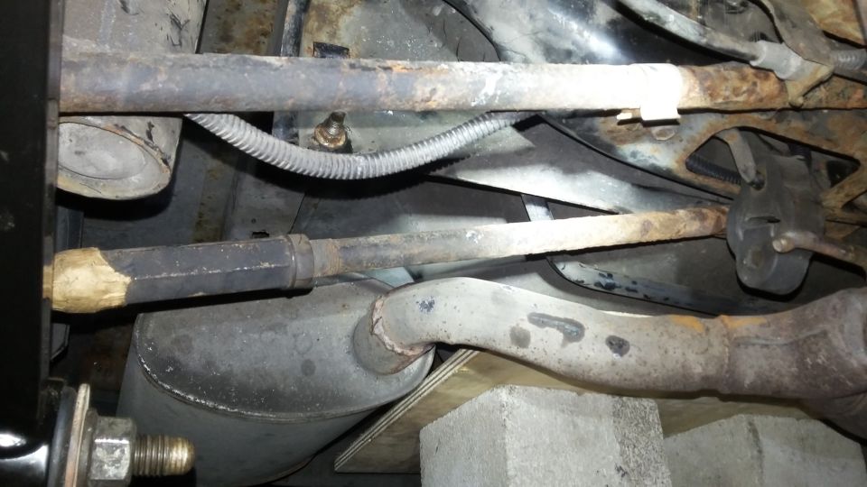 Undercarriage of a vehicle with rusted suspension components and exhaust system supported by concrete blocks