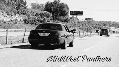 2004 Ford Crown Victoria - A black sedan drives down a highway with other vehicles in traffic. A billboard is visible in the background.