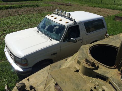1993 Ford Bronco - A white 1993 Ford Bronco is parked outdoors next to a military vehicle.