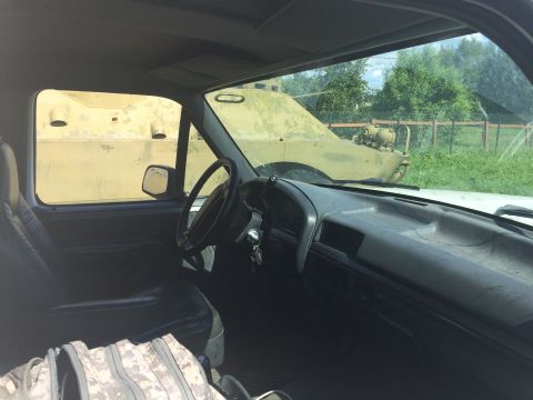 1993 Ford Bronco - View from inside a truck cab shows a military vehicle parked in a grassy area.