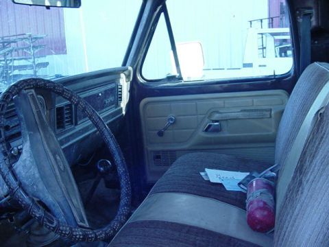 1992 Ford Bronco - The interior of an older truck, a worn steering wheel and fabric seats. A fire extinguisher is visible on the passenger seat.