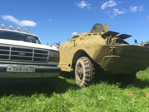 1993 Ford Bronco - A white Ford truck is parked next to a military armored vehicle under a blue sky.