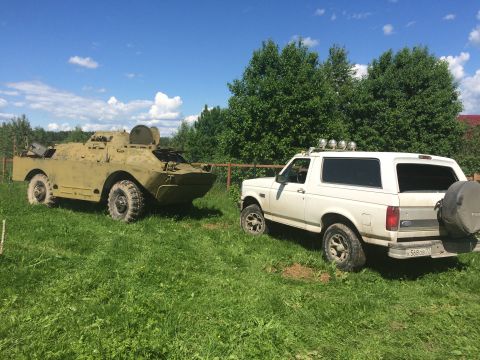 1993 Ford Bronco - A white 1993 Ford Bronco is parked on a grassy field next to a military vehicle under a blue sky.