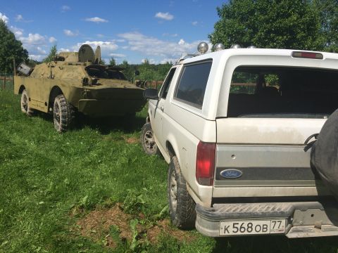 1993 Ford Bronco - A 1993 Ford Bronco is parked in a field next to a military vehicle under a blue sky.