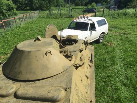 1993 Ford Bronco - A white SUV with roof lights sits in a yard next to a camouflaged military vehicle.