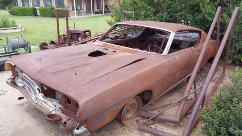 1973 Ford F-100 - This heavily rusted coupe sits in a yard, showing significant damage to its body and missing parts.