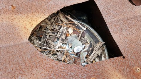 1973 Ford F-100 - A hole in rusted metal reveals debris and a wheel rim, suggesting a discarded vehicle part.