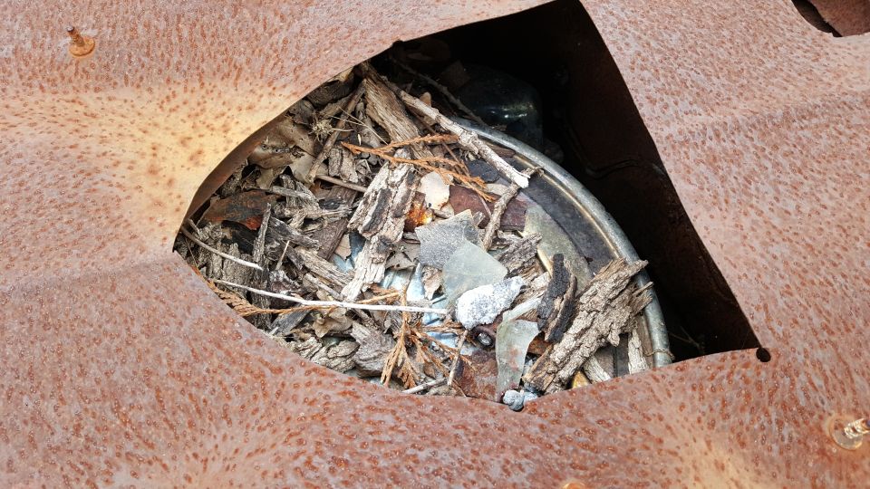 Rusted metal panel with debris inside a hole, showing a glimpse of a wheel rim